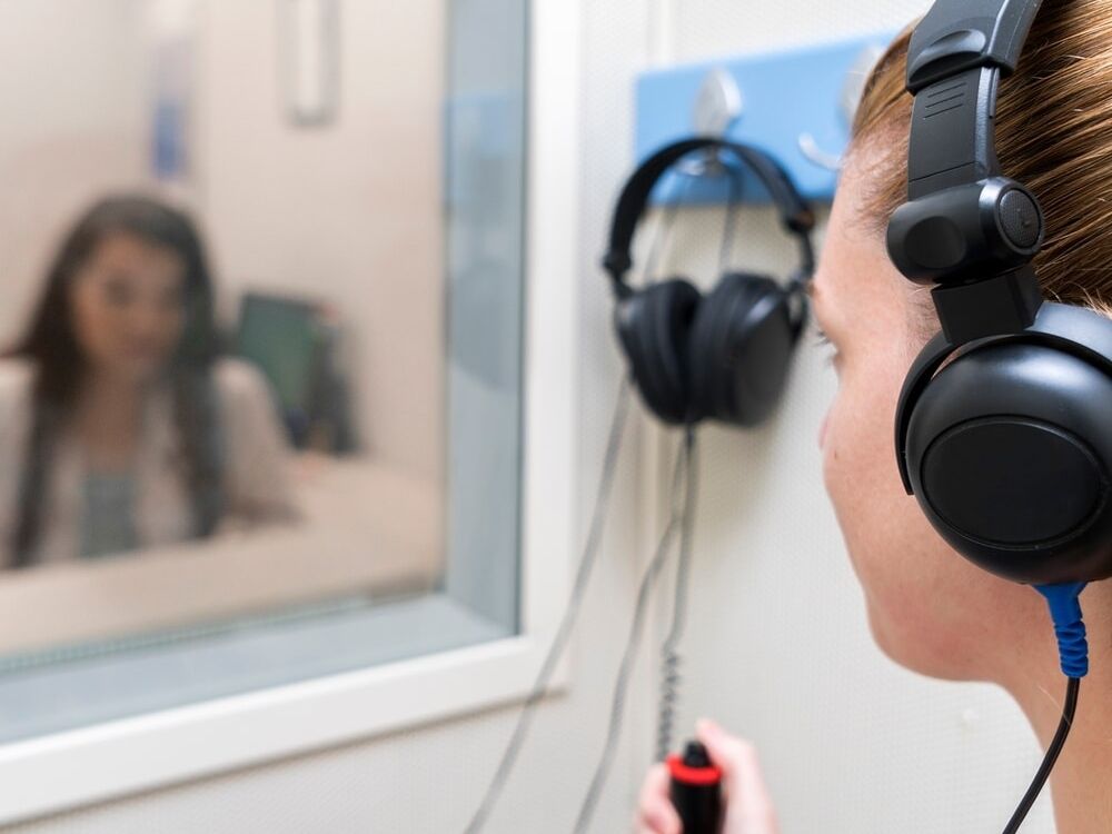 Doctor of Audiology performing a hearing test in a sound booth at Optimum Audiology in Apple Valley, CA