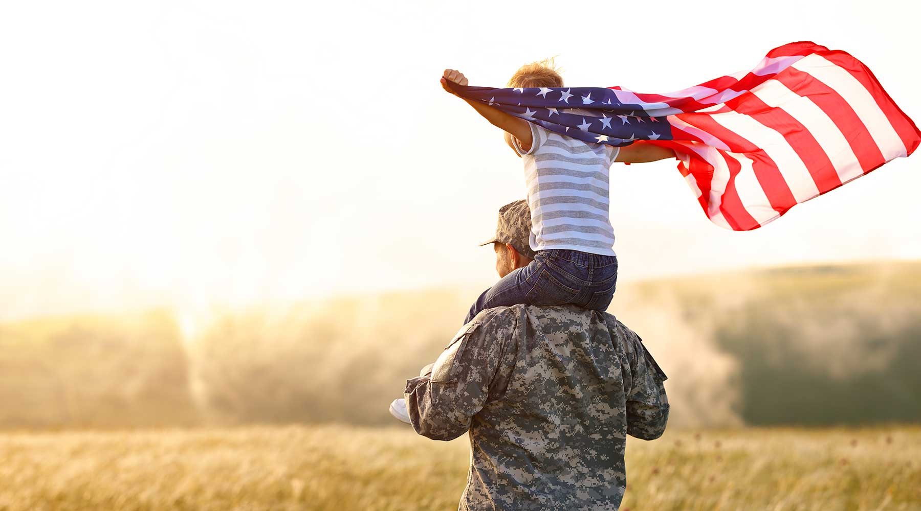 Veteran with his grandson on his shoulders holding an American flag.